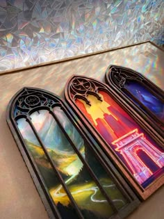 three stained glass windows sitting next to each other on top of a table in front of a wall