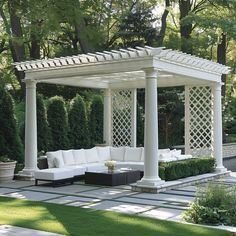 a white couch sitting under a pergoline covered gazebo in the middle of a lush green park