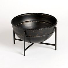 a black metal bowl sitting on top of a table next to a wooden stand with two legs