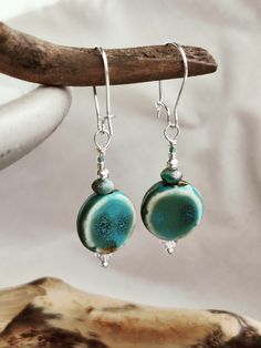 the earrings are made with blue and green glass beads on silver earwires, hanging from a branch