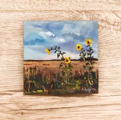 a painting of sunflowers in a field on a wooden surface with blue sky and clouds