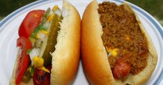 two hot dogs on buns with chili, peppers and relish sitting on a plate