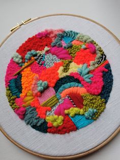 a colorful circular design on a white wall hanging in front of a wooden hoop frame