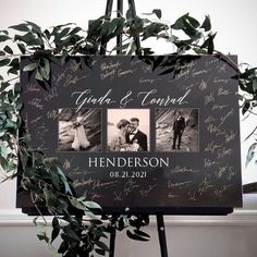 a couple's wedding photo on a sign surrounded by leaves and greenery in front of a white wall