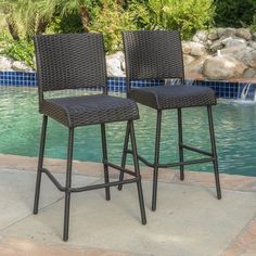 two brown wicker barstools next to a pool with water fountain in the background