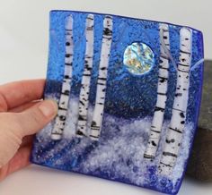 a hand holding a blue glass plate with white birch trees in the snow on it