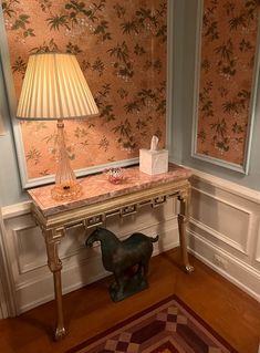 a small table with a lamp on it in front of a wallpapered room