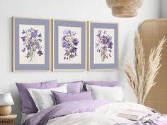 a bed with purple and white sheets in a bedroom next to two pictures on the wall