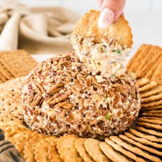 a cracker being dipped with cheese and nuts on top of a platter of crackers