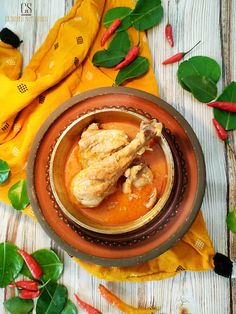 a bowl filled with chicken and sauce on top of a yellow cloth next to green leaves