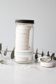 a jar filled with lots of white buttons next to some green leaves on a table