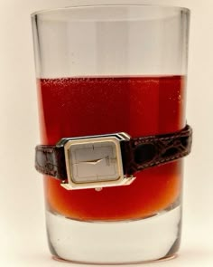 a glass filled with liquid and a watch on the strap around it's wrist