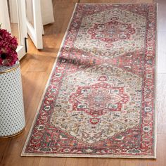 a red and beige rug on the floor next to a vase with flowers in it