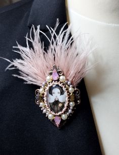 a pink brooch with an image of a woman in pearls and feathers on it