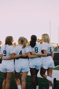 a group of women in white soccer uniforms huddle together at the end of a field