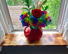 a red vase filled with colorful flowers on top of a window sill