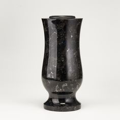 a black marble vase sitting on top of a white table next to a gray wall