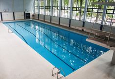 an indoor swimming pool with ladders and windows on the wall, in a building