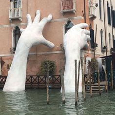 two giant white hands sticking out of the water in front of a building with windows and balconies