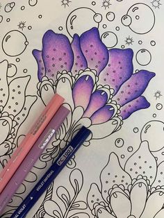 two pencils sitting on top of an adult coloring book with flowers and bubbles in the background