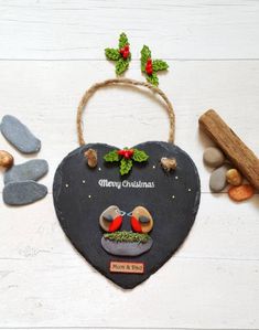 a slate heart with two birds and holly leaves on it, surrounded by stones and wood