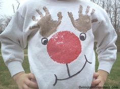 a young boy wearing a reindeer sweater with his hands on his face and nose painted onto it