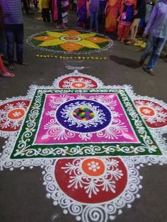 people are standing around and looking at colorful rangolii designs on the ground in front of them