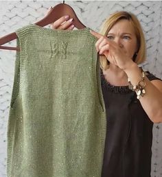 a woman pointing at a green sweater hanging on a clothes hanger in front of a white wall