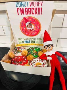 an elf is sitting next to a box of doughnuts