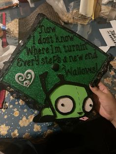 someone is holding up a graduation cap decorated with green and black frosting that says, not what i know when i'm trim every steps in new on halloween