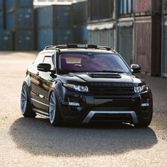 a black range rover parked in front of some shipping containers