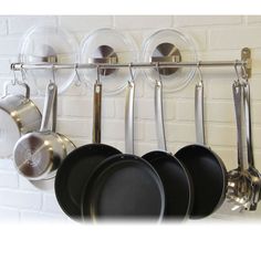 pots and pans are hanging on a rack in front of a white brick wall