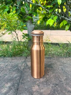 a metal bottle sitting on the ground in front of some trees