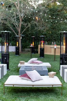 an outdoor lounge set up in the grass with lights strung above it and pillows on top