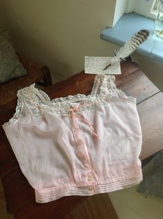 a cotton and lace camisole in a pink color with coral pink silk ribbon, and beautiful buttons. there is a little faded stain at the front ( photo 7.) in excellent condition bust 88 cm  34.5" waist 63 cm 24 3/4" Fitted Pink Top With Delicate Lace, Fitted Pink Delicate Lace Top, Fitted Pink Camisole With Lace Top, Pink Fitted Lace Top Camisole, Fitted Lace Top Pink Camisole, Pink Cotton Camisole With Lace Trim, Pink Lace Top For Wedding, Vintage Camisole Top For Daywear, Fitted Pink Camisole With Delicate Lace