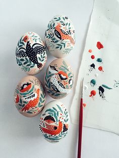 an assortment of painted eggs sitting on top of a white surface next to a brush