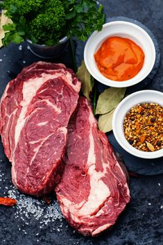 raw meat with spices and seasoning next to it on a black surface, including carrots