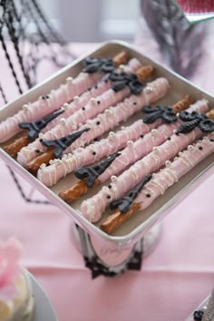 there are many pink and black donuts in the tray on the cake table with other desserts