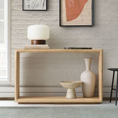 two vases are sitting on a shelf in front of a brick wall with framed pictures above it