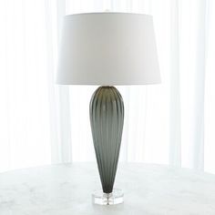 a table lamp sitting on top of a white table next to a curtained window