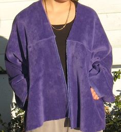 a woman standing in front of a white house wearing a purple jacket and black top