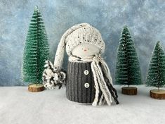 a knitted doll is standing in the snow next to small trees