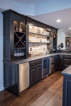 a large kitchen with black cabinets and stainless steel appliances in the center, along with wooden flooring