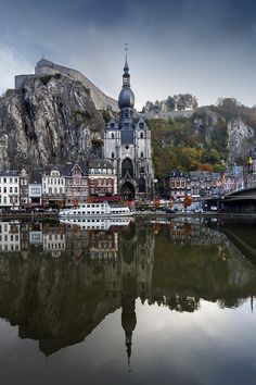 an old town is reflected in the still waters of a river with mountains in the background