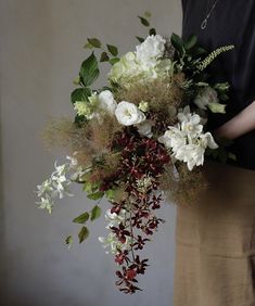 a woman holding a bouquet of white and red flowers with greenery in her hands