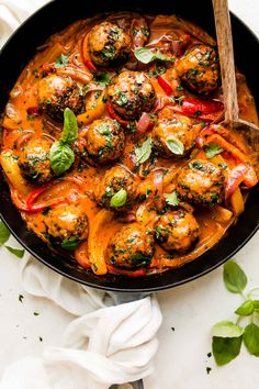 a skillet filled with meatballs and vegetables covered in sauce, garnished with fresh herbs