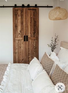 a bed with white linens and pillows in front of a wooden door that is open