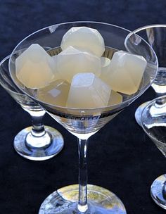 three martini glasses filled with ice cubes on a black tableclothed surface,