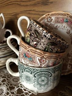 a stack of coffee cups sitting on top of a table next to lace doily