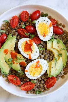 a white plate topped with an egg, avocado and tomato salad on top of lentils